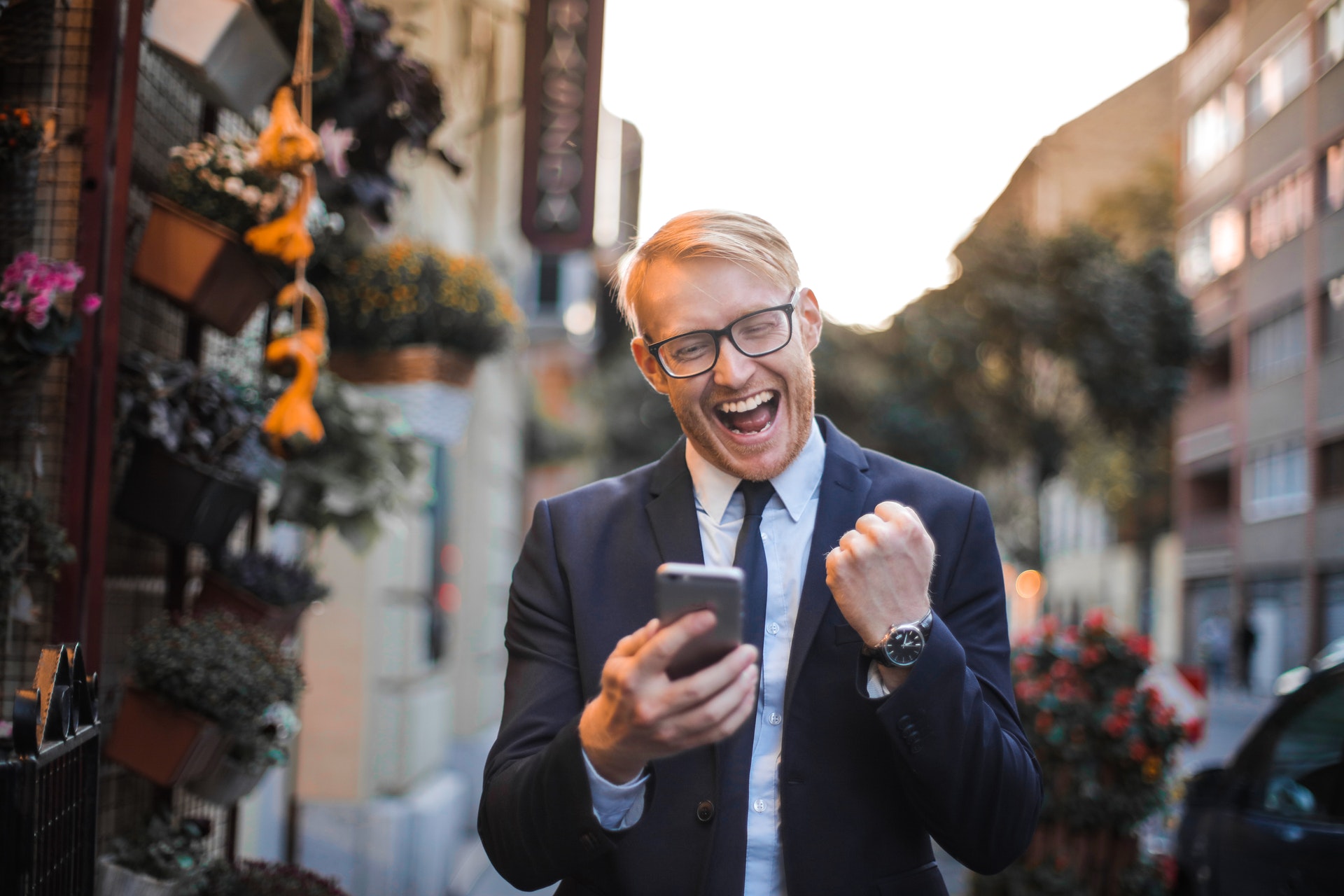 Imagem de um homem de terno com o celular na mão e comemorando. Imagem ilustrativa texto negócios promissores.