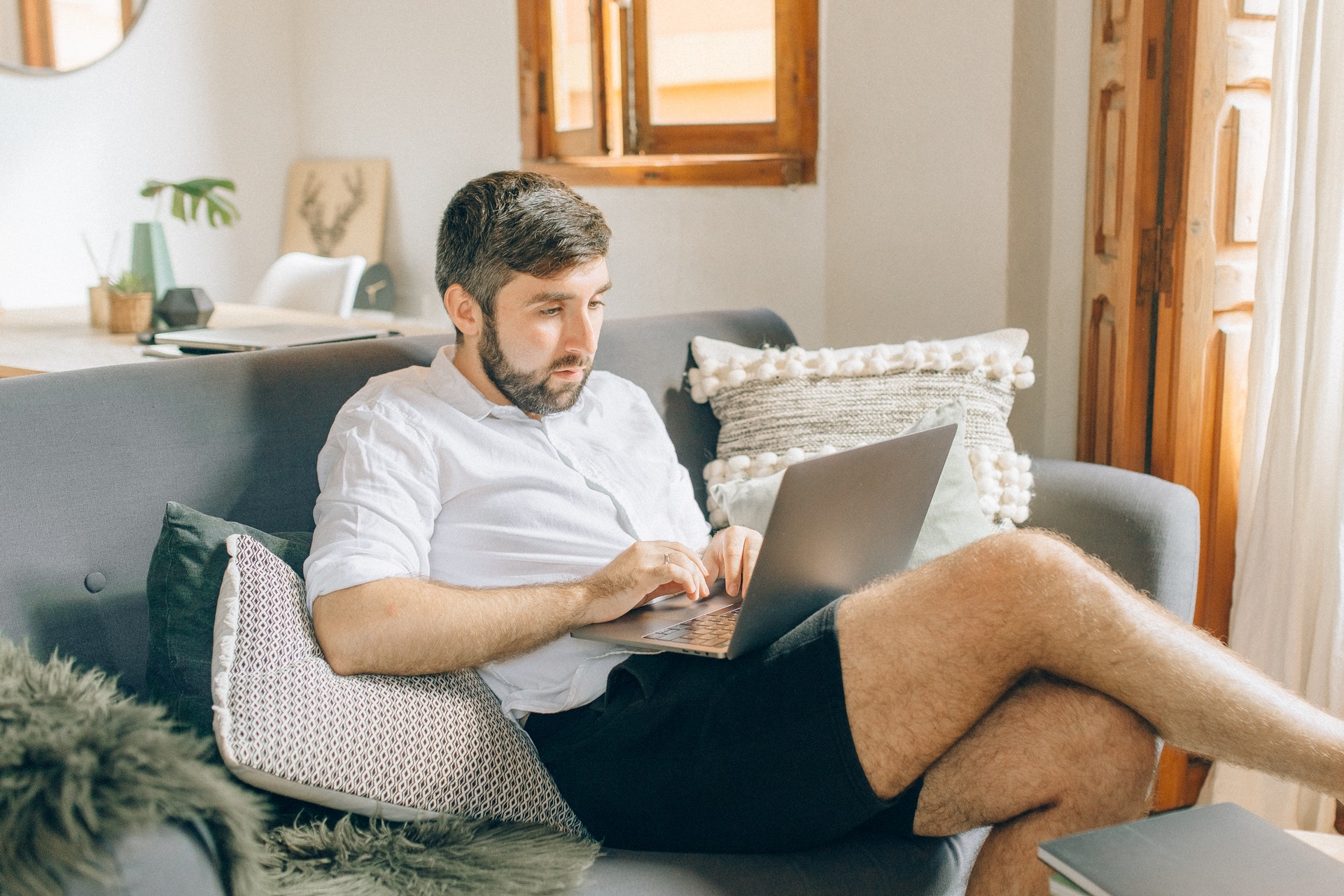 Imagem de um homem no sofá de casa trabalhando em um computador. Imagem ilustrativa texto tipo de negócio é mais rentável.