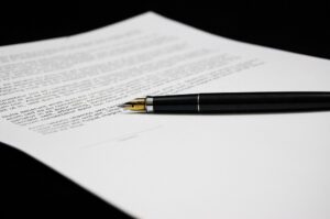 Imagem de um contrato com uma caneta de cabo preto por cima dele. Imagem ilustrativa texto cláusula arbitral em contrato de franquias.