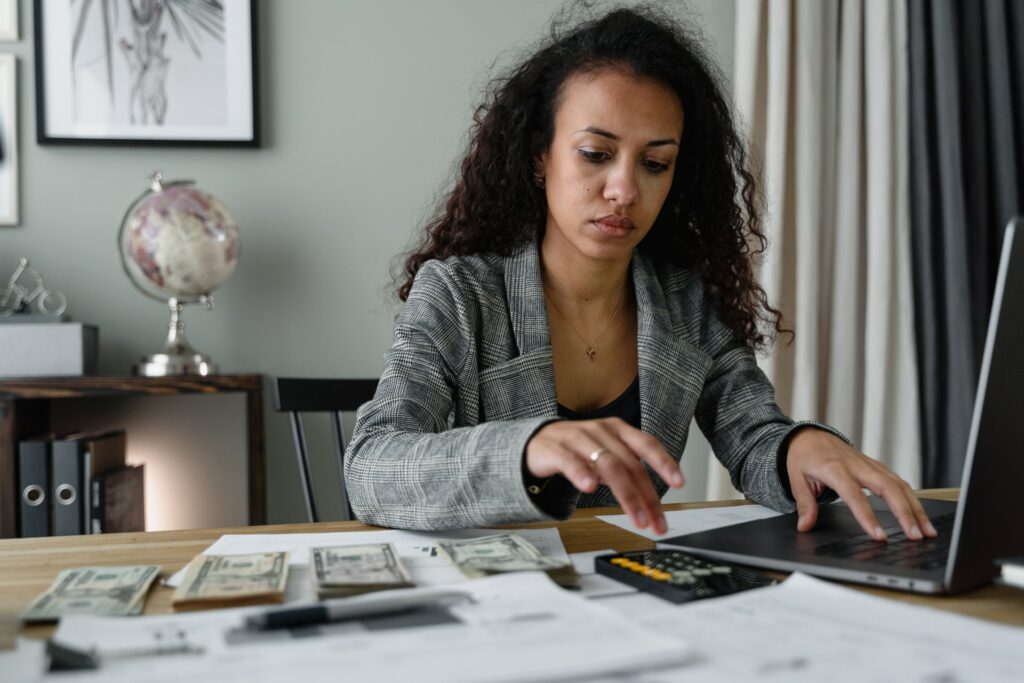 Imagem de uma mulher em uma mesa olhando para o computador e fazendo cálculos em uma calculadora, ao lado de notas de dinheiro. Imagem ilustrativa texto franquia perfeita.