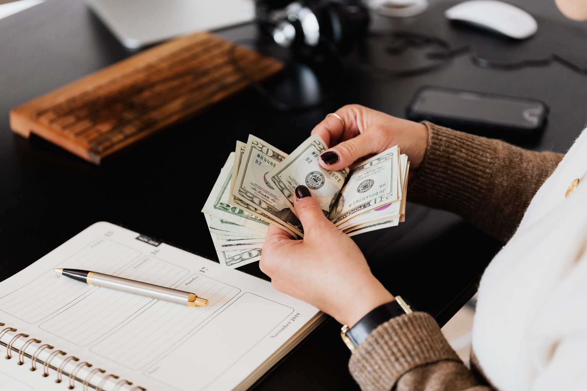 Imagem de uma pessoa contando dinheiro em uma mesa com um caderno e uma caneta. Imagem ilustrativa texto investimentos a longo prazo.