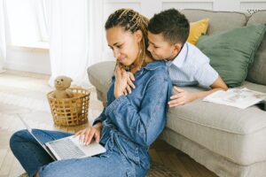 Imagem de uma mulher usando o computador com o seu filho a abraçando. Imagem ilustrativa texto mães empreendedoras.