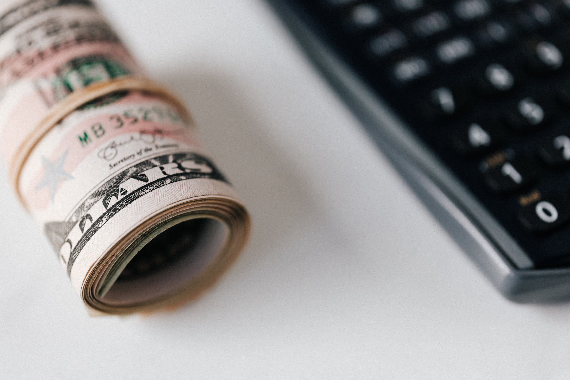 Imagem de notas de dinheiro em formato de tubo e uma calculadora. Imagem ilustrativa texto melhor ideia de negócio.
