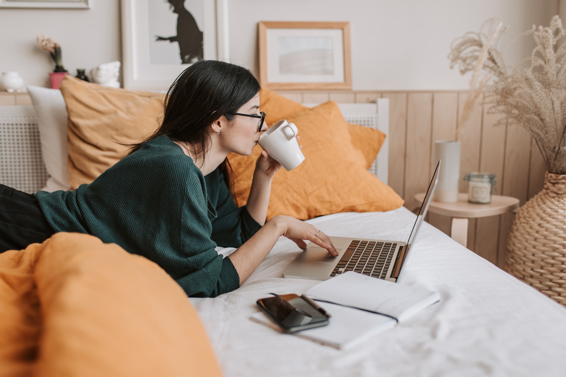 Imagem de uma mulher deitada na cama bebendo algo em uma caneca e olhando para o computador. Imagem ilustrativa texto nichos promissores.