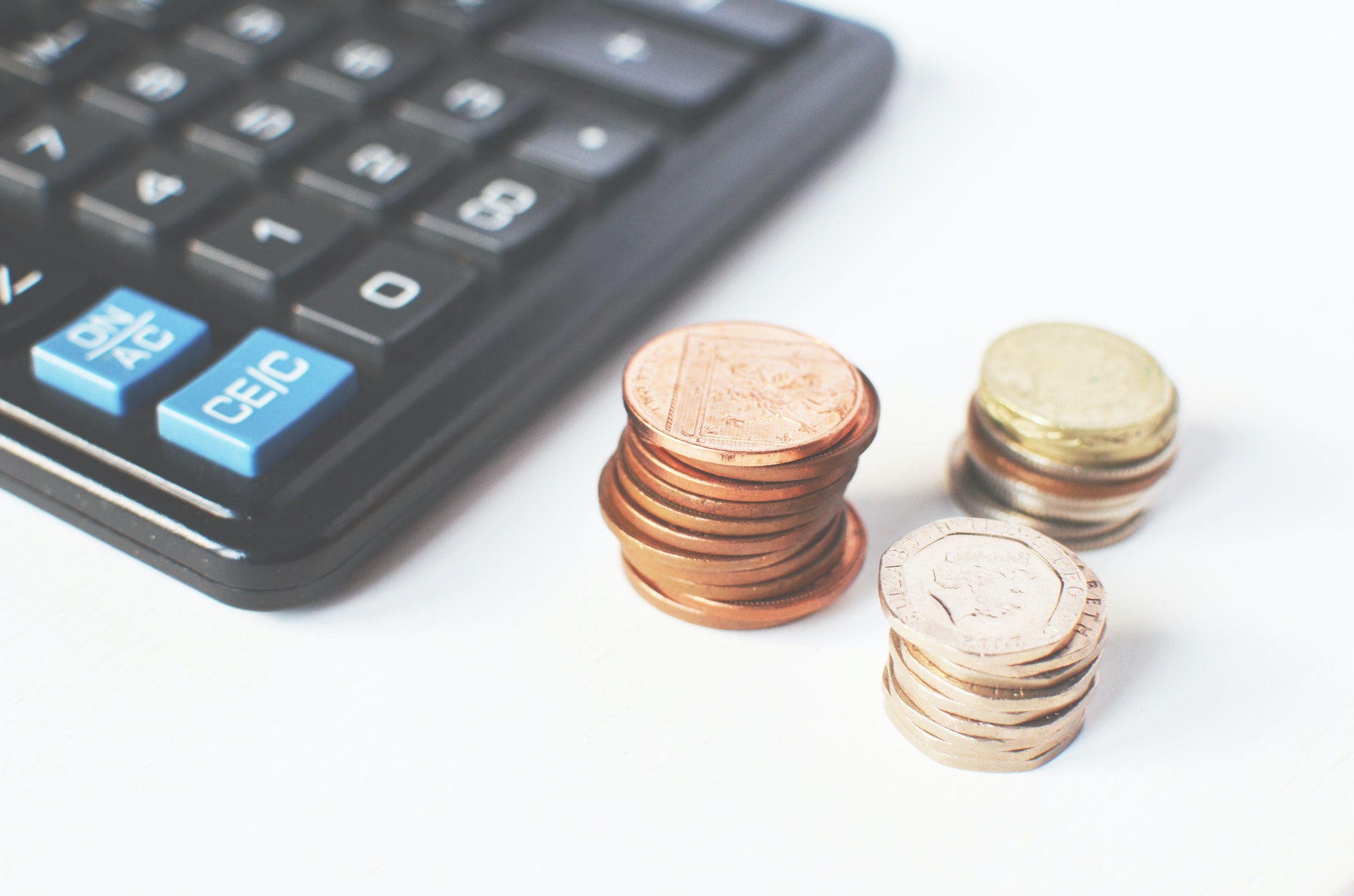 Imagem de três pilhas de moedas perto de uma calculadora. Imagem ilustrativa texto segmentos de franquias com baixo investimento.