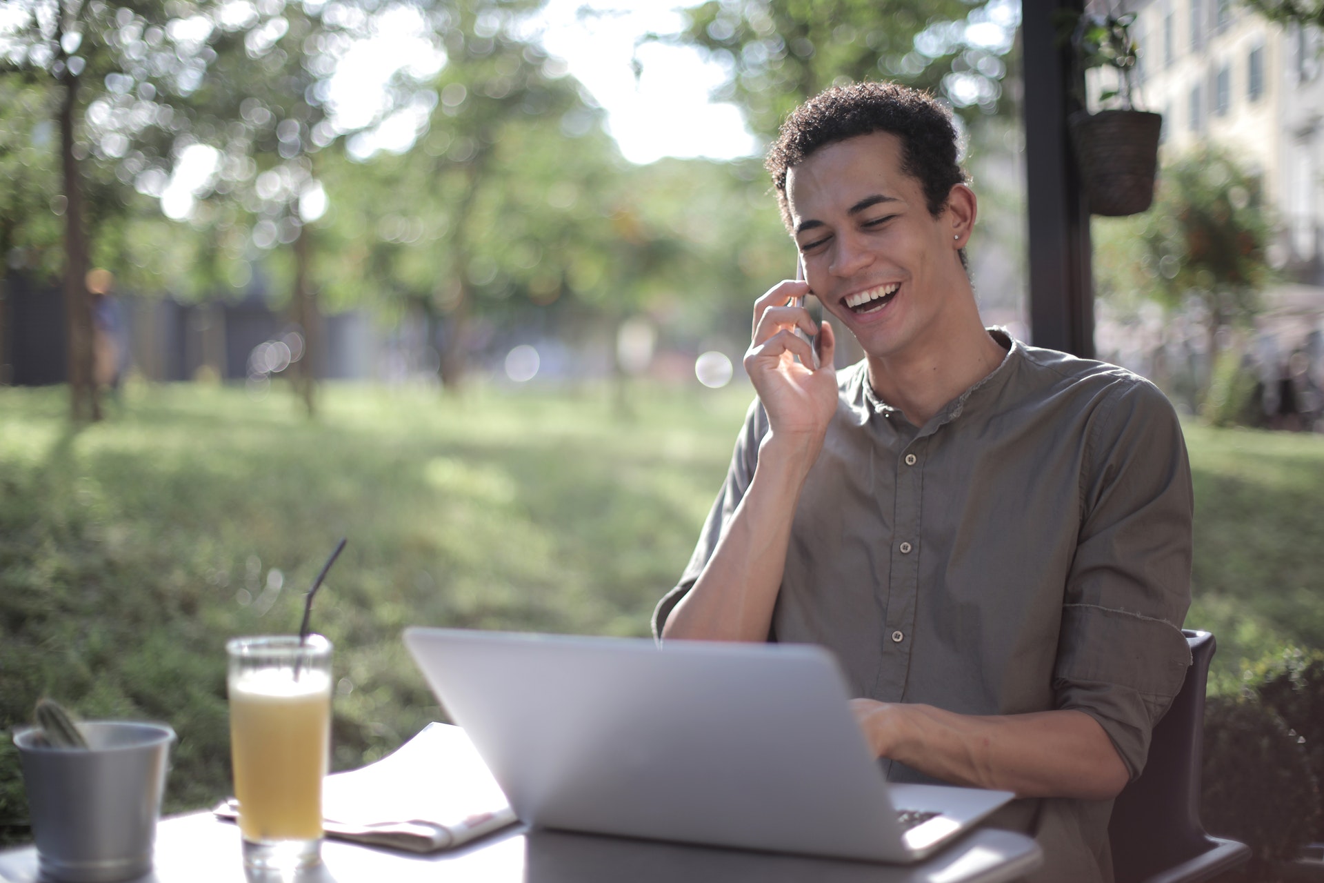Imagem de um empresário sorrindo sentando em frente um computador em uma mesa ao ar livre. Imagem ilustrativa texto dono de franquia ou negócio próprio.