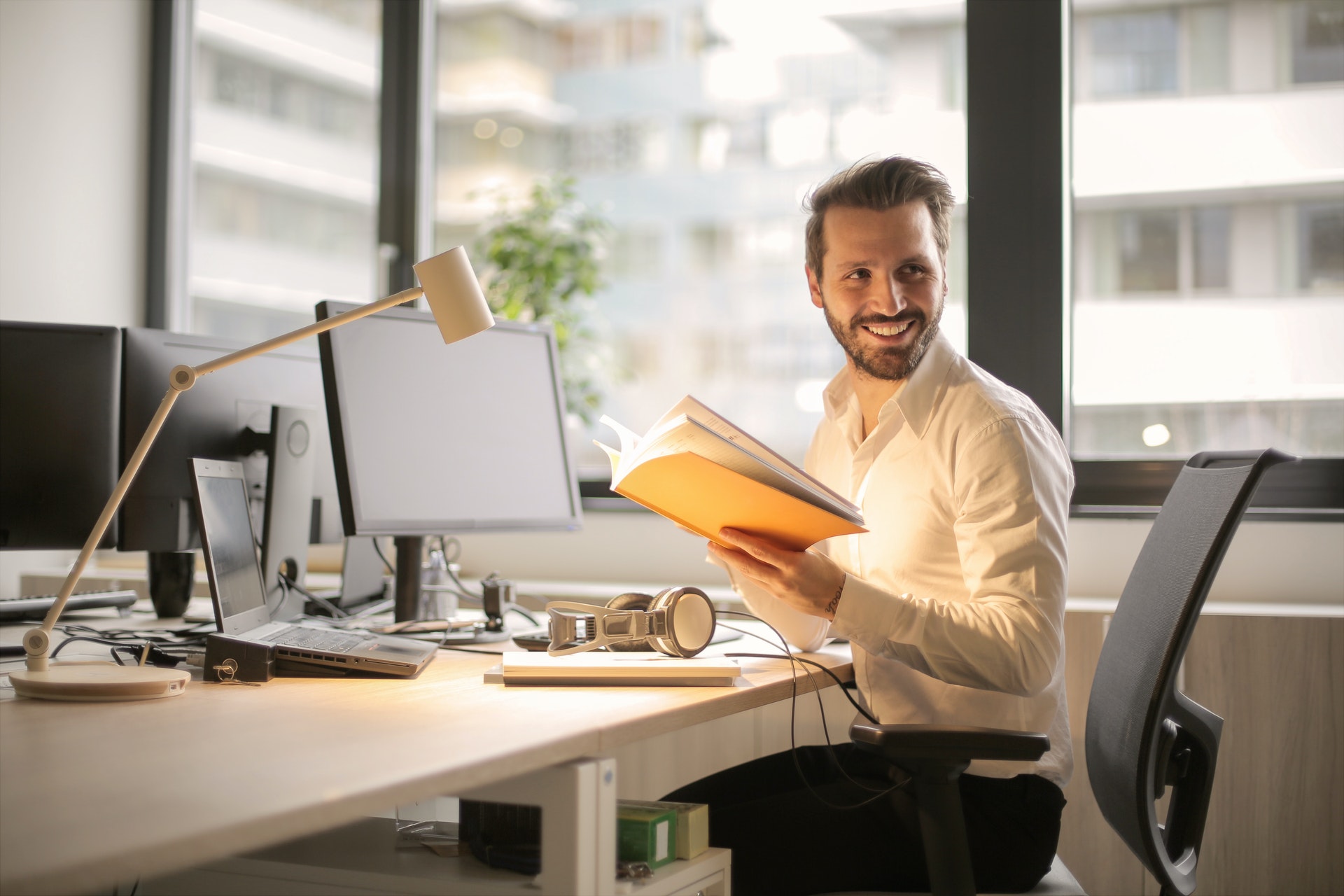 Imagem de um empresário em uma mesa de escritório com papeis e um computador. Ele está sorrindo e segurando uma pasta. Imagem ilustrativa texto expandir seu negócio.