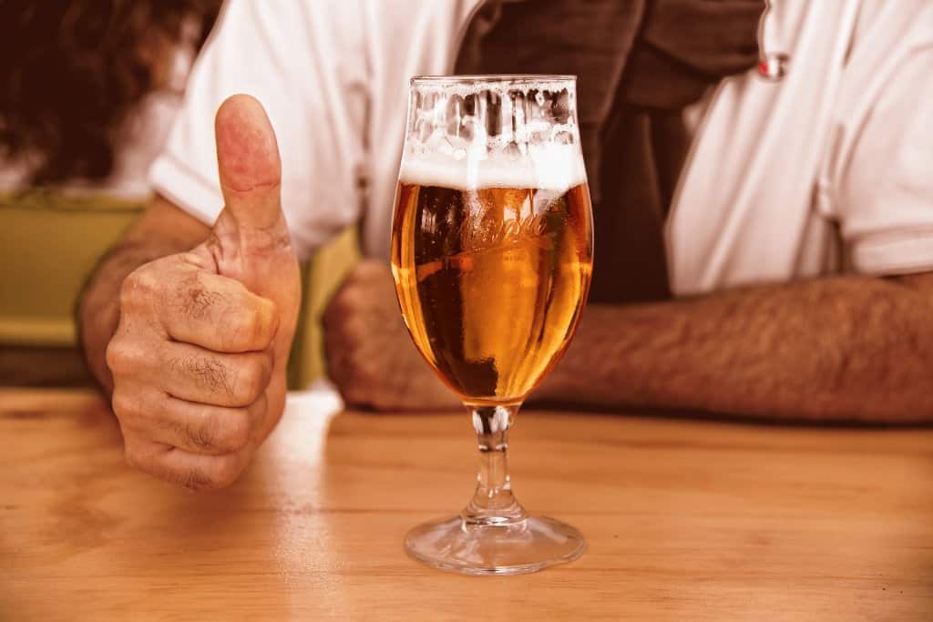 Foto de pessoa e um copo com cerveja. Imagem ilustrativa para texto franquia de bebidas bar do urso.