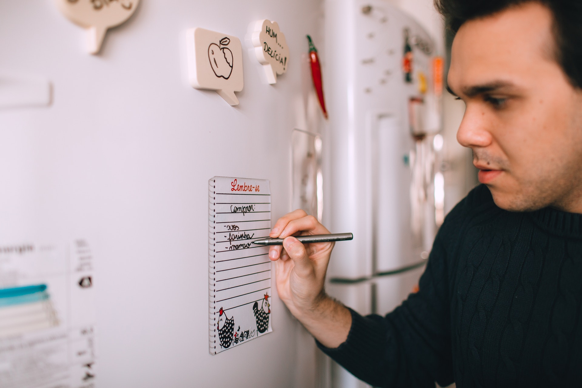 Imagem de um homem escrevendo em um papel de anotações na porta de uma geladeira. Imagem ilustrativa texto franquias com retorno rápido.
