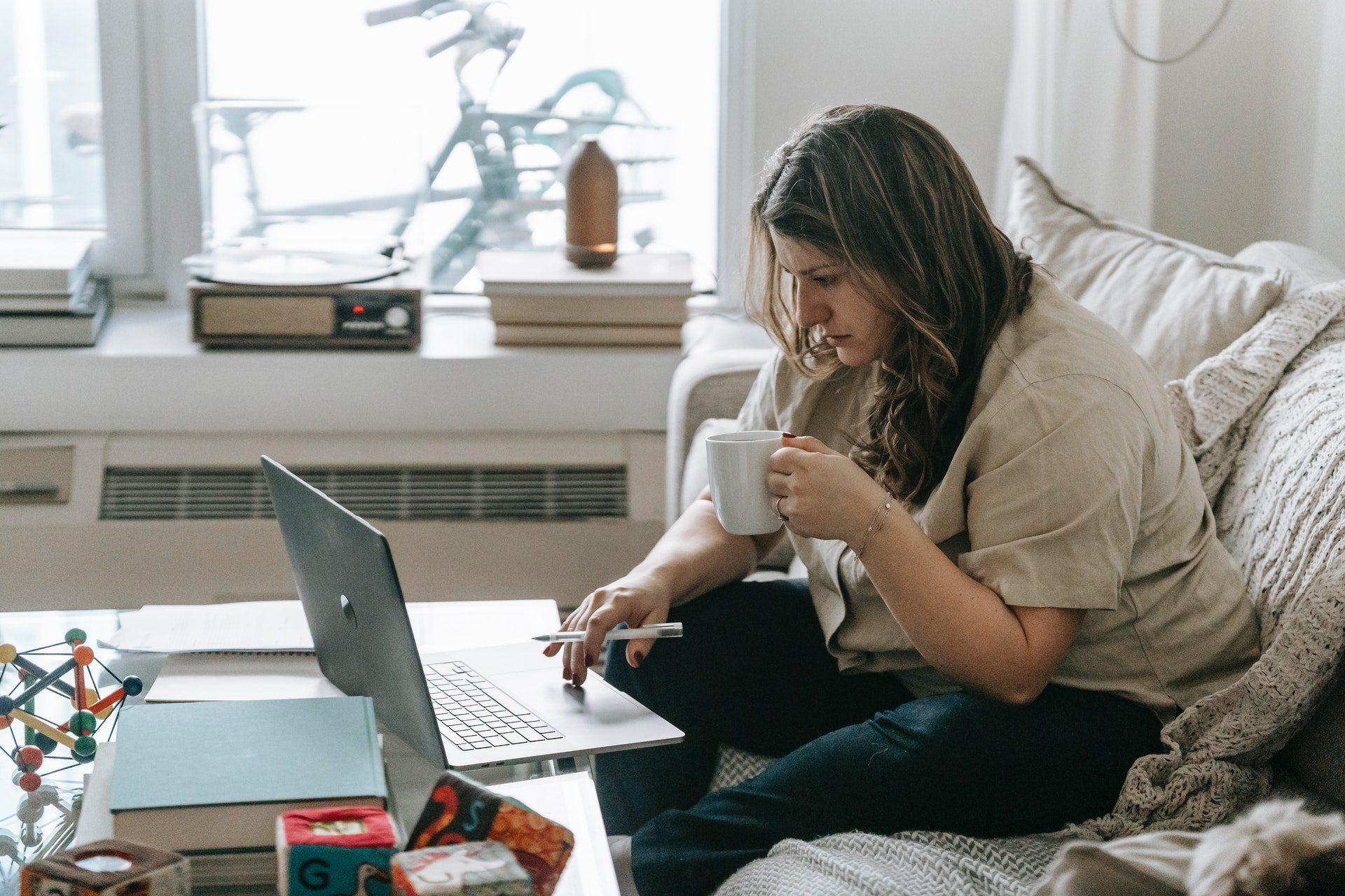 Mulher olhando um computador sentada no sofá de casa com uma xícara na mão. Imagem ilustrativa do texto o que é ser empreendedor.