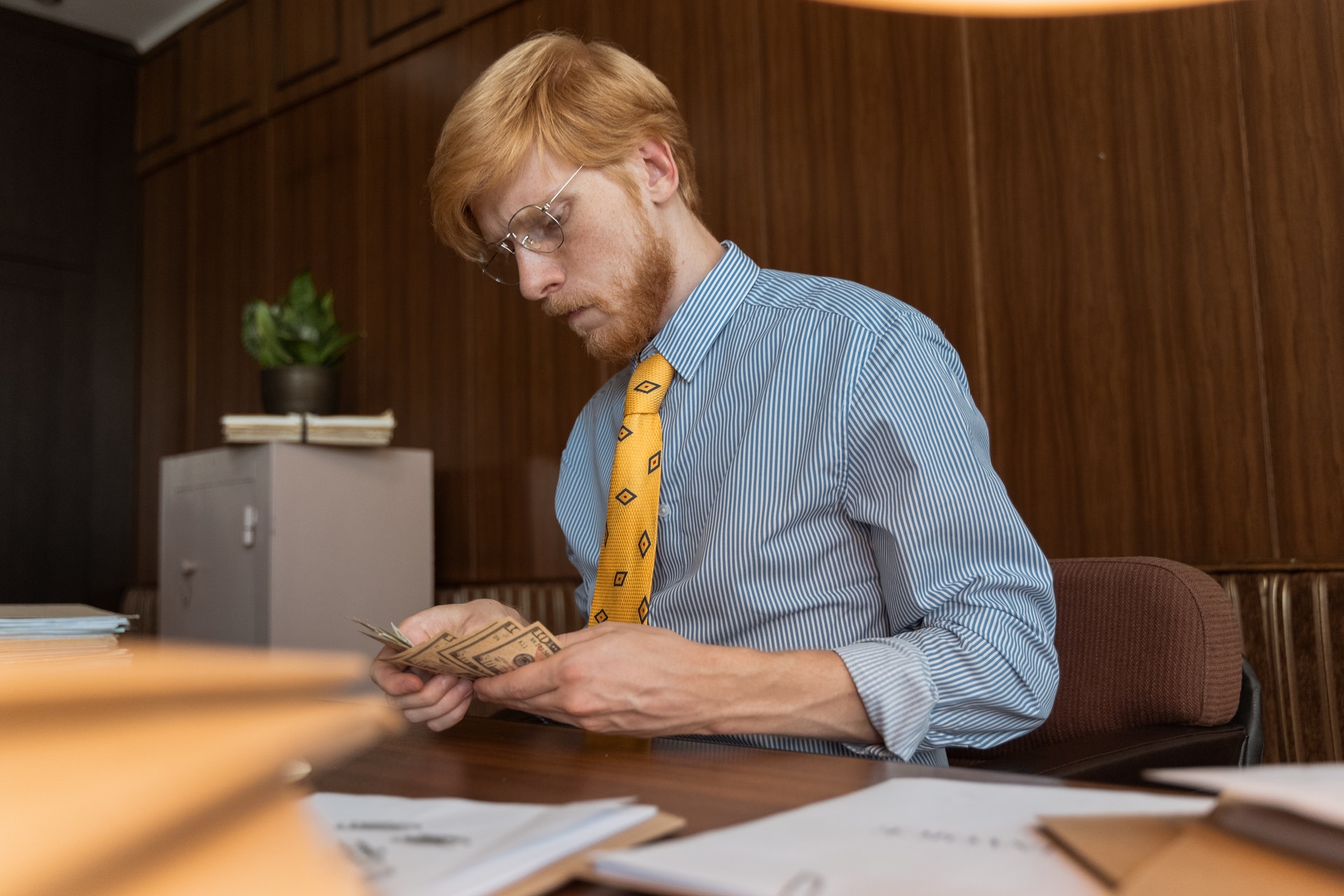 Imagem de um homem de negócios segurando algumas notas de dinheiro em uma mesa de escritório. Imagem ilustrativa texto franquias baratas 2022.