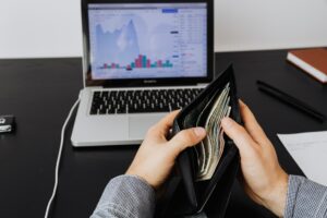 Imagem de um computador com gráficos e de duas mãos segurando uma carteira cheia de dinheiro. Imagem ilustrativa do texto franquias lucrativas 2022.