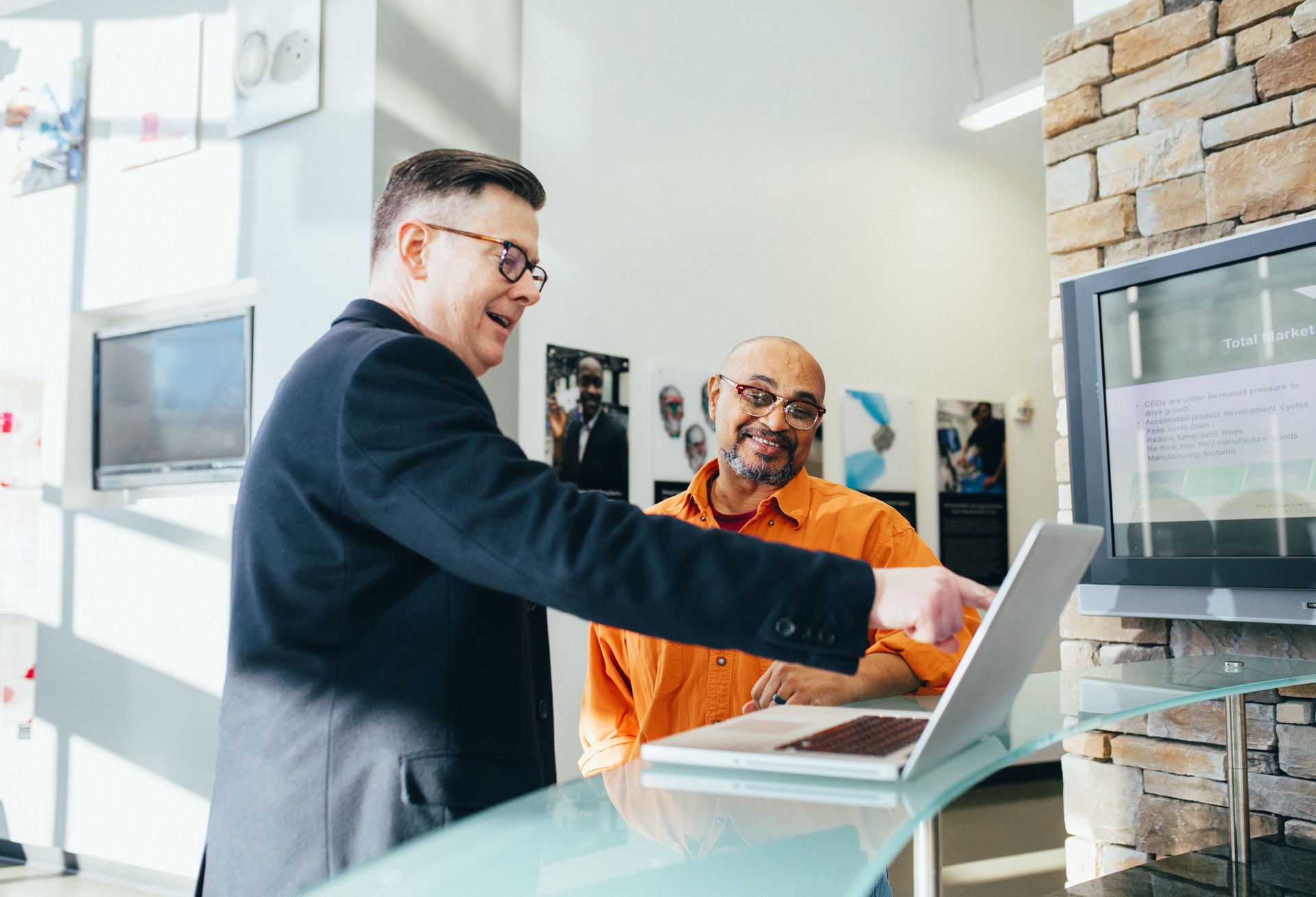 Imagem de um empreendedor sorrindo apontando para um computador junto a outro homem. Imagem ilustrativa do texto grandes empreendimentos.