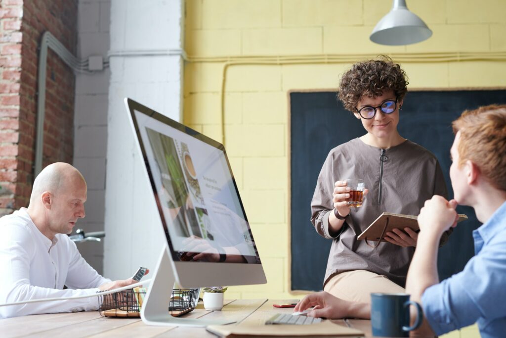 Imagem de uma pessoa em frente a um computador conversando com outra em um escritório. Imagem ilustrativa texto o que preciso para abrir uma corretora de seguros.
