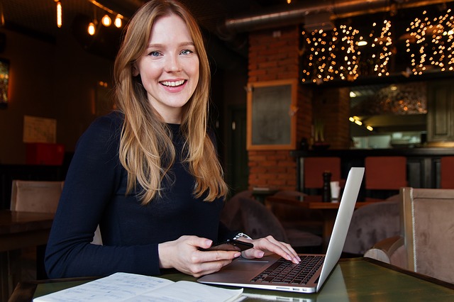 Mulher jovem usando um computador e sorrindo. Ilustração do texto sobre investimento para iniciantes.