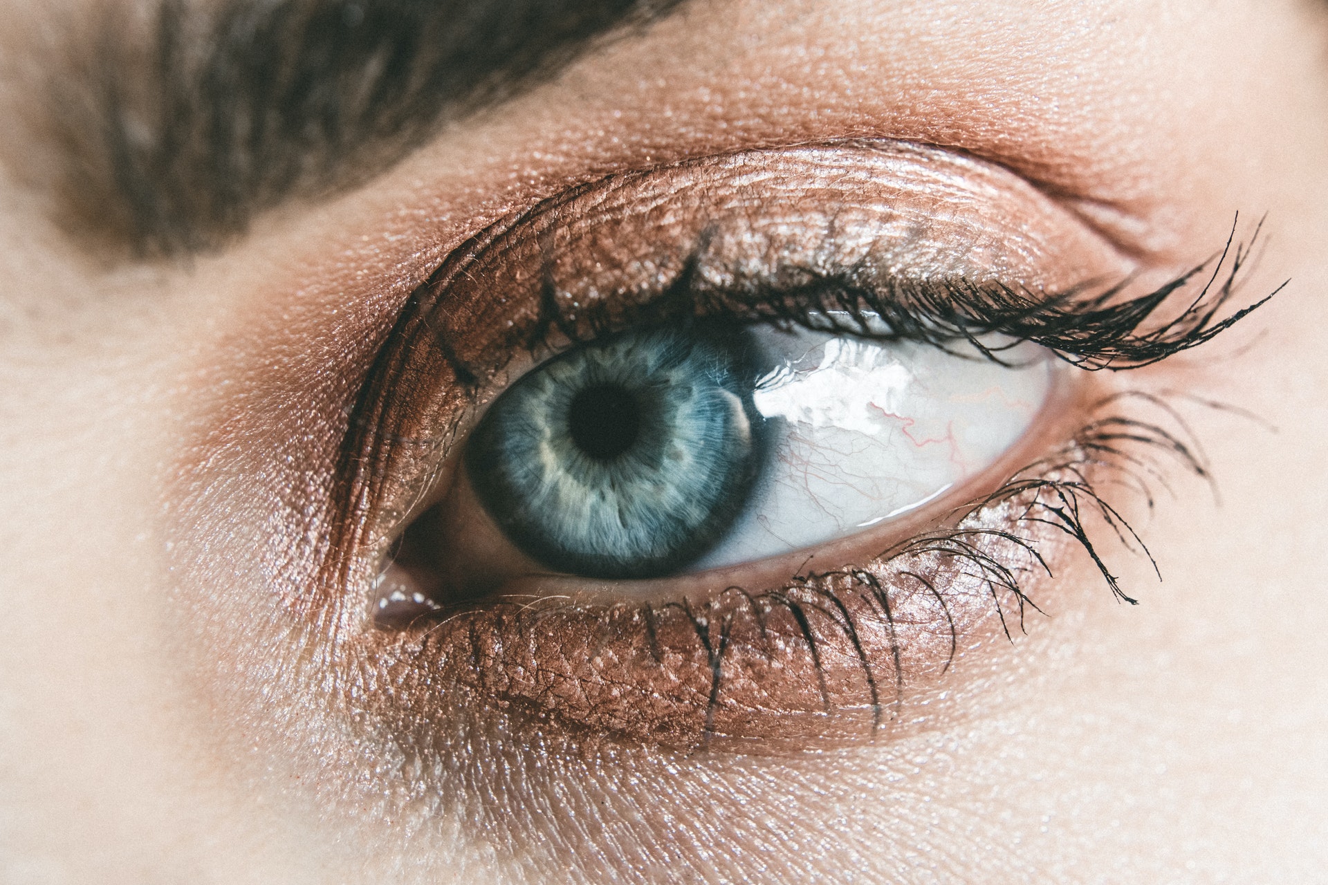 Imagem de perto de um olho azul, com cílios delineados. 