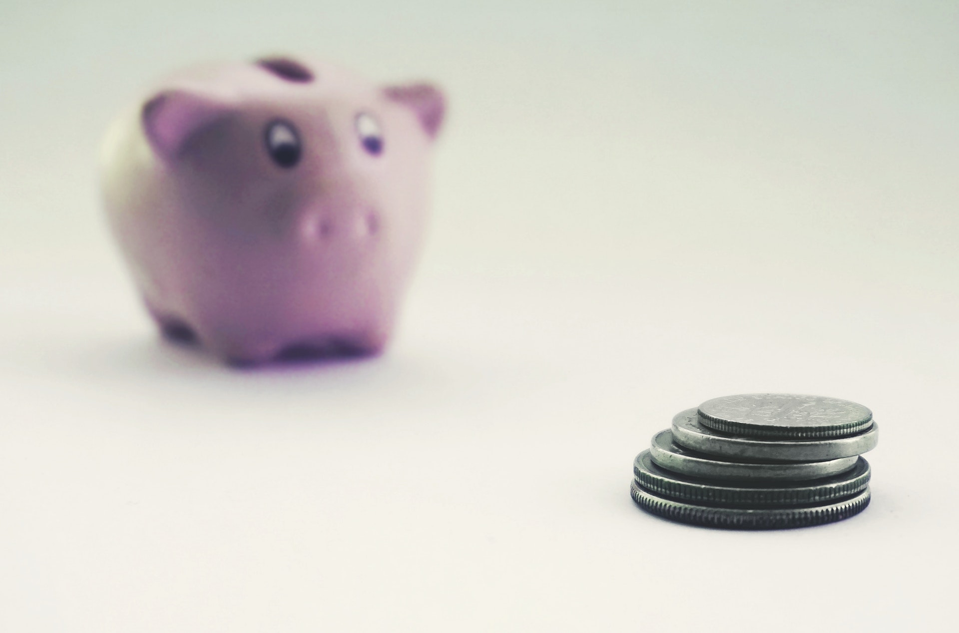 Imagem de um cofre em formato de porco e um pequeno monte de moedas. 