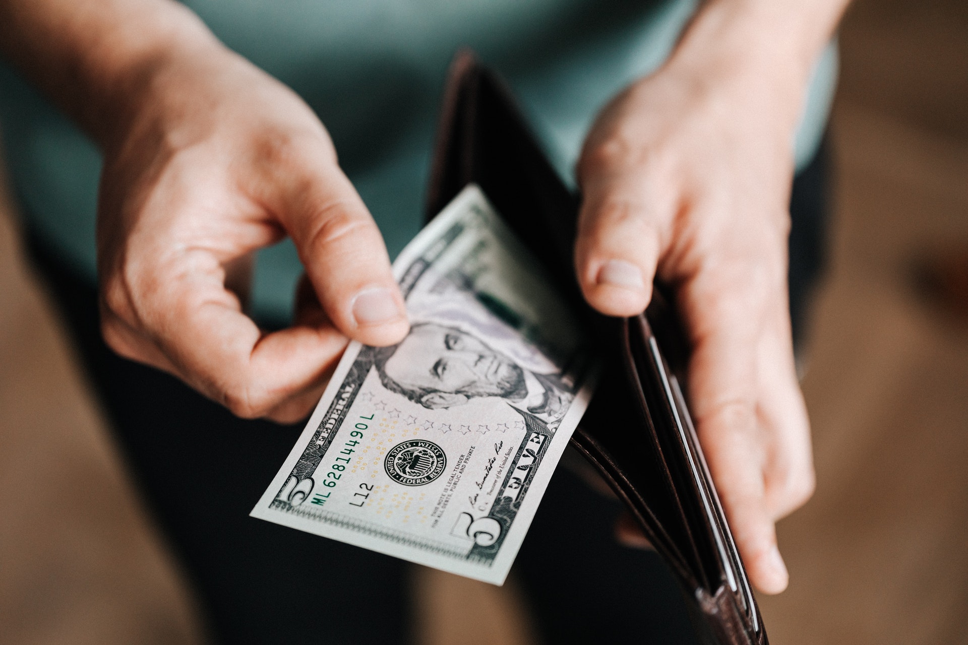 Pessoa segurando uma carteira e tirando uma nota de dólar dela. Imagem ilustrativa do texto como ter independência financeira com franquia.