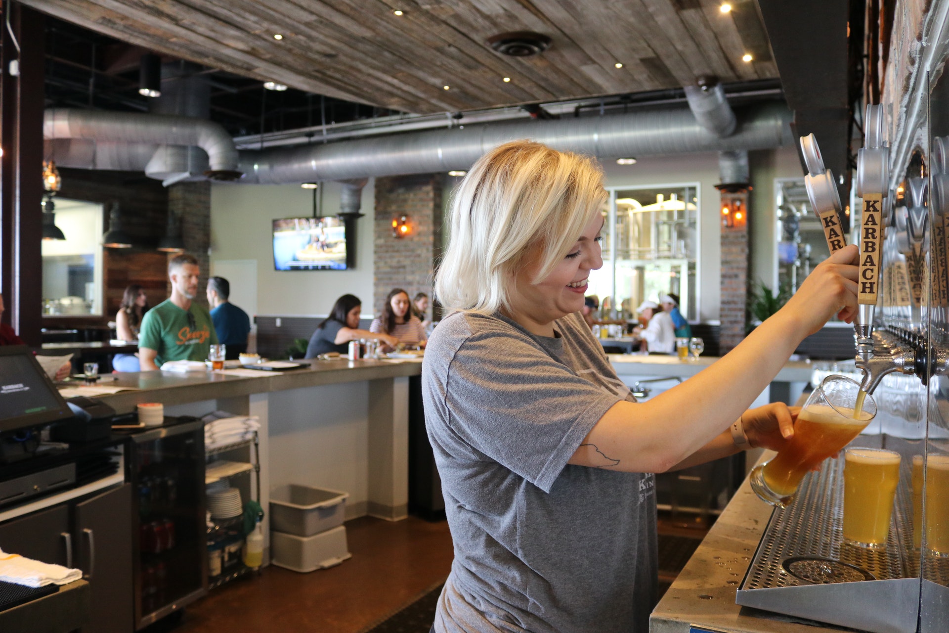 Mulher servindo um copo de chopp e um cliente esperando no balcão do bar. 