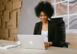 Mulher de casaco preto sorri enquanto olha para o notebook. Imagem ilustrativa texto montar um negocio dicas.