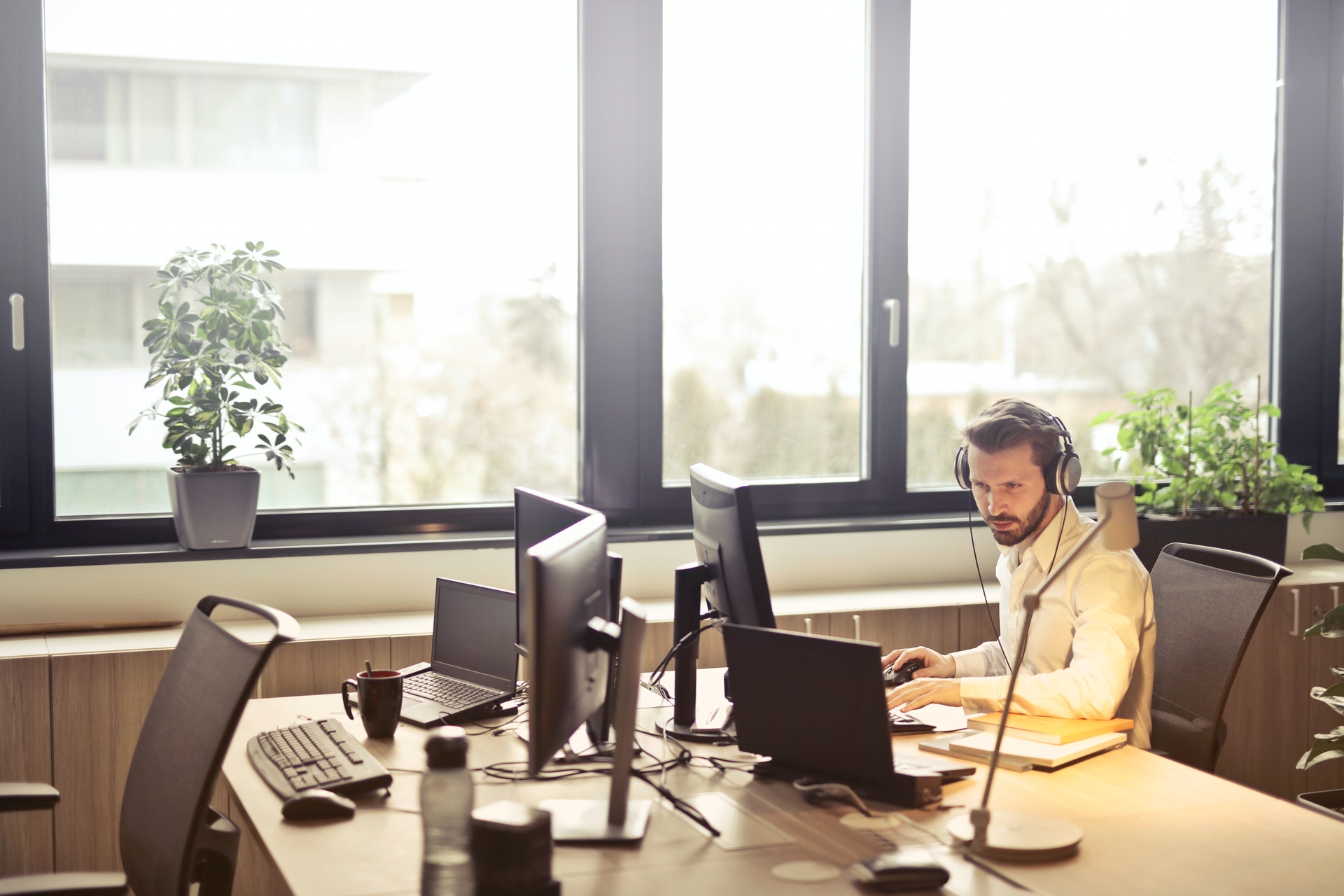 Empresário trabalhando em uma mesa de escritório com computadores e usando um fone de ouvido. Imagem ilustrativa do texto montar um negócio, dicas.