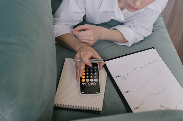 Pessoa deitada de bruços em um sofá fazendo conta na calculadora do celular. Ilustração do texto sobre empreendedor de sucesso com pouco dinheiro.
