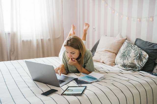 Mulher de bruços em cama usando computador e tablet. Ilustração do texto sobre empreender com pouco dinheiro.
