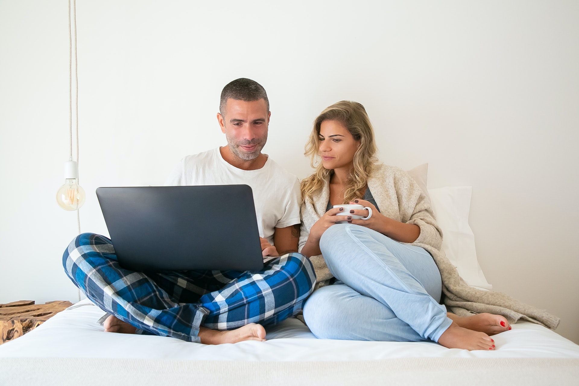 Casal na cama olhando para o computador. Imagem ilustrativa do texto franquia sem sair de casa.