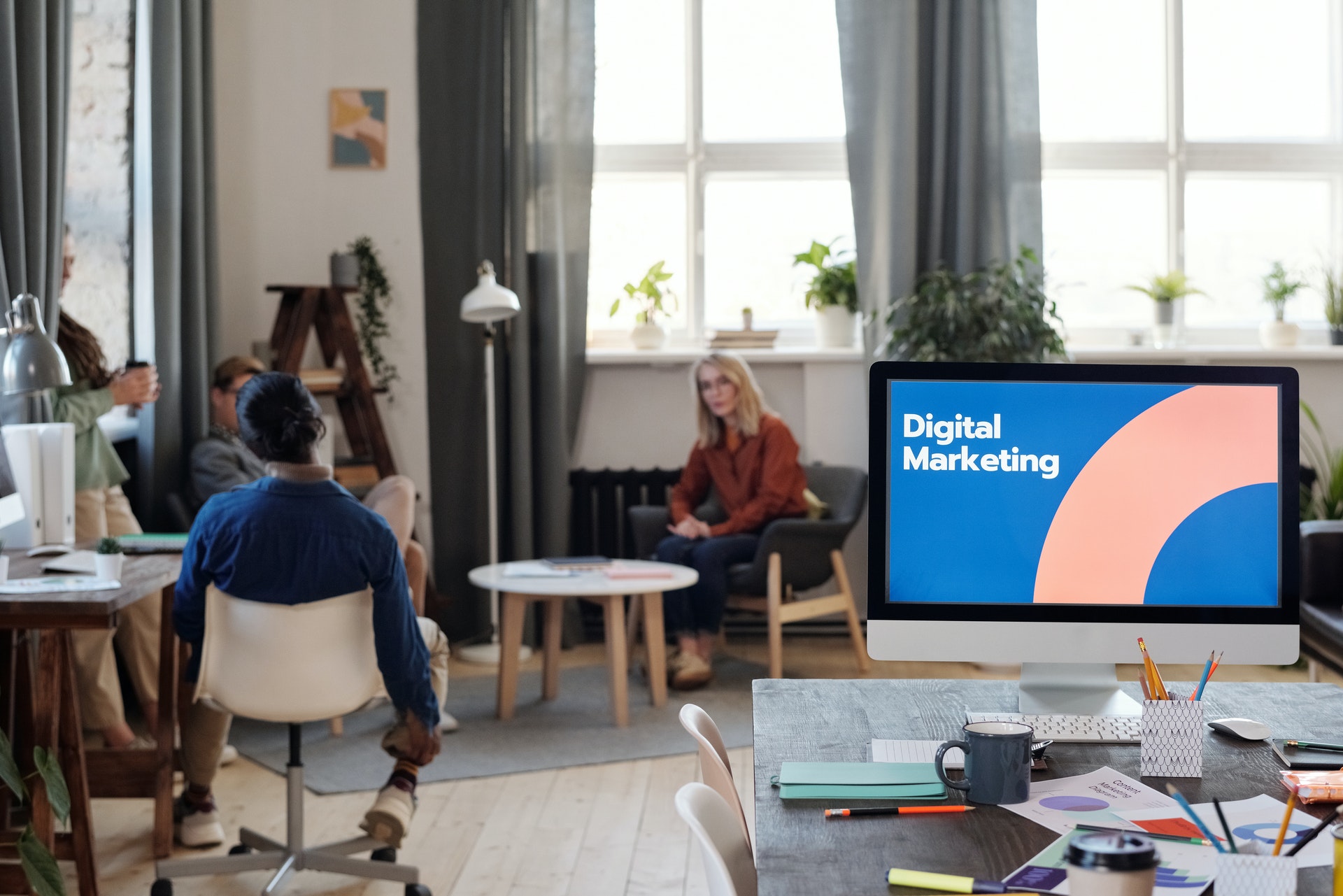 Sala com pessoas e um computador na mesa com os escritos Digital Marketing na tela. 