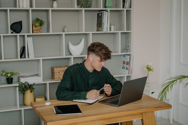 Imagem de um homem sentado em mesa de madeira em frente a computador. Imagem ilustrativa texto micro empreendedor individual.