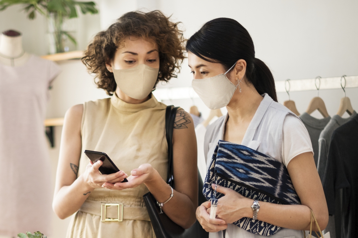 duas mulheres de máscara olhando celular em loja ilustração de negócios-lucrativos-com-pouco-investimento