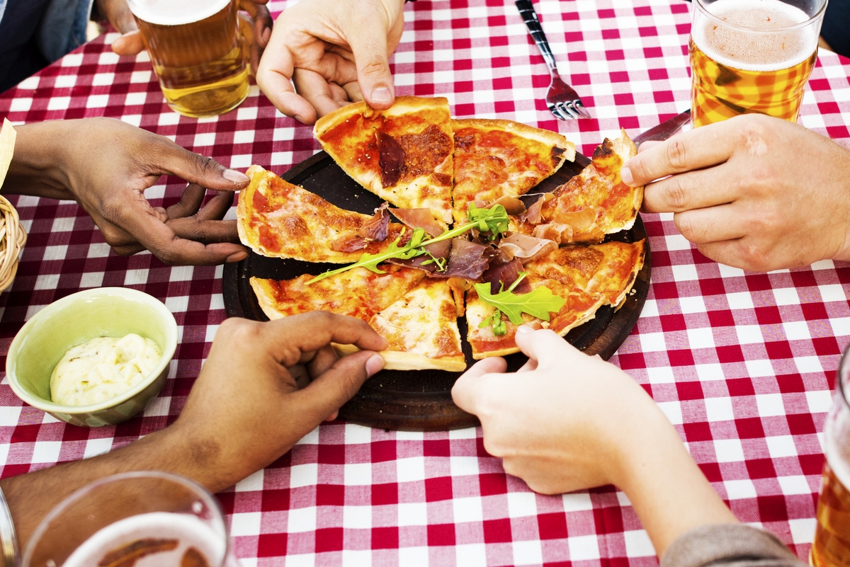 Pessoas dividindo pizza em mesa ao lado de copos de cerveja. Ilustração do texto sobre opção de empreendimentos.