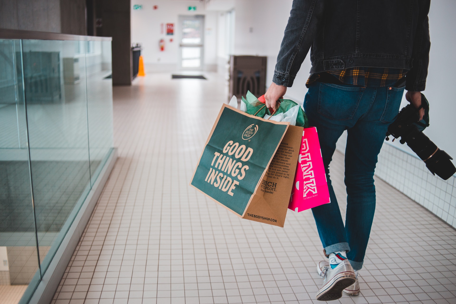 Pessoa segurando sacolas de compras em uma mão e uma máquina fotográfica na outra. Imagem ilustrativa do texto por que investir em franquia.