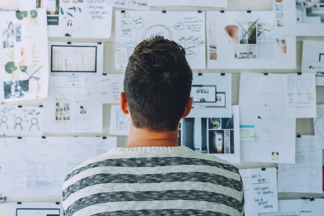 Homem olhando para papéis colados em uma parede com gráficos. Ilustração do texto vida de empreendedor.
