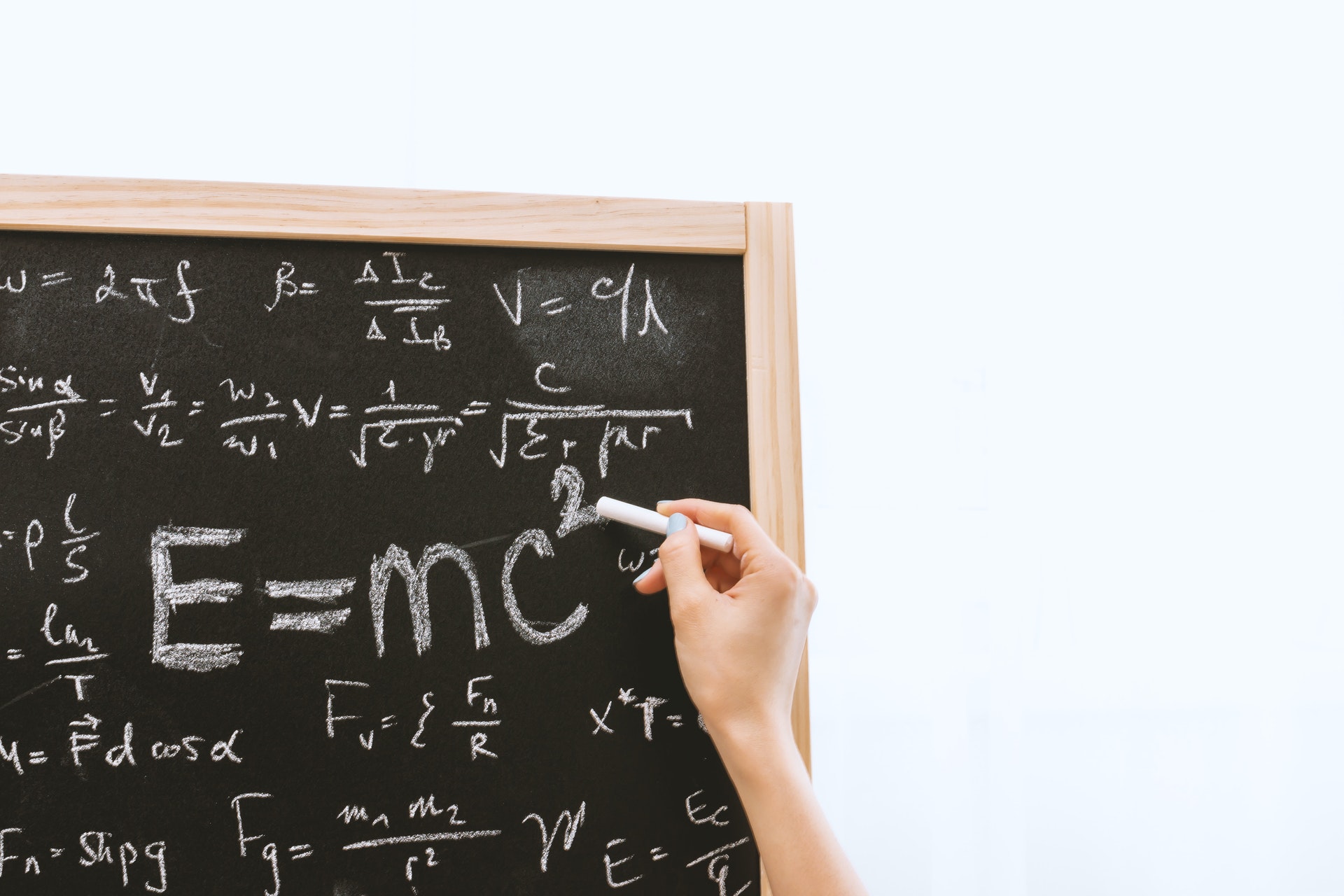 Mão escrevendo em um quadro com um giz e várias fórmulas matemáticas no quadro. Imagem ilustrativa do texto curso de matemática para crianças.