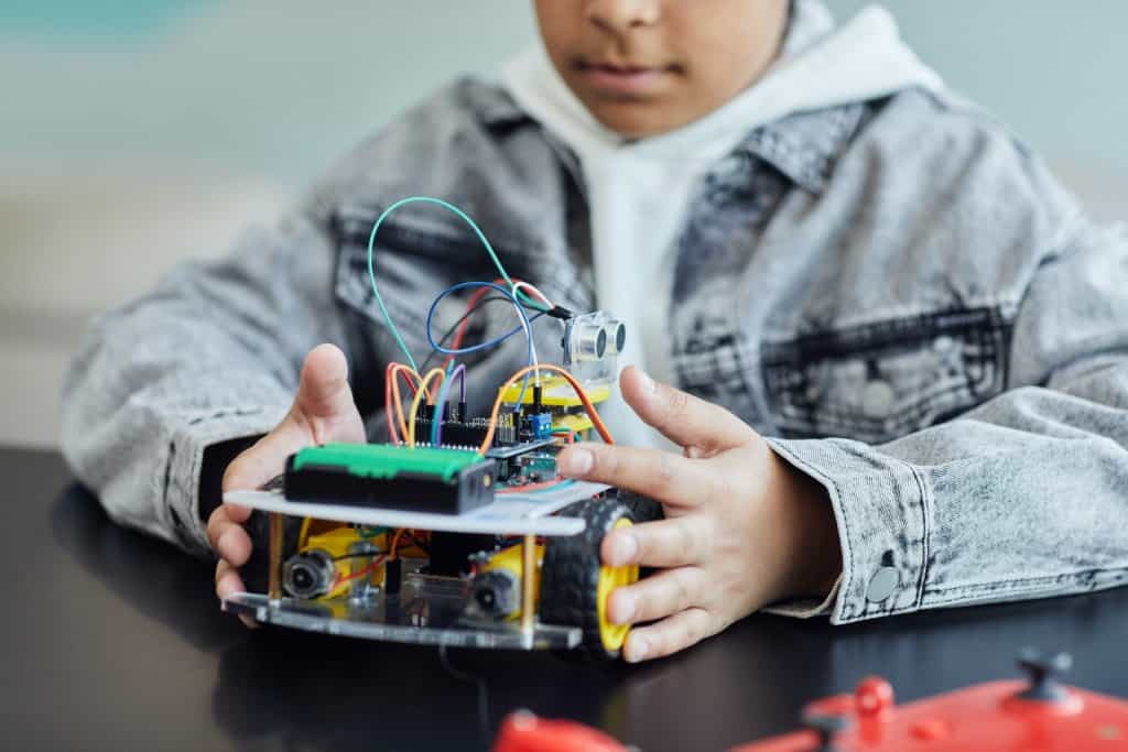 Imagem de uma criança com um pequeno protótipo de robô. Imagem ilustrativa texto curso de robótica e programação infantil.
