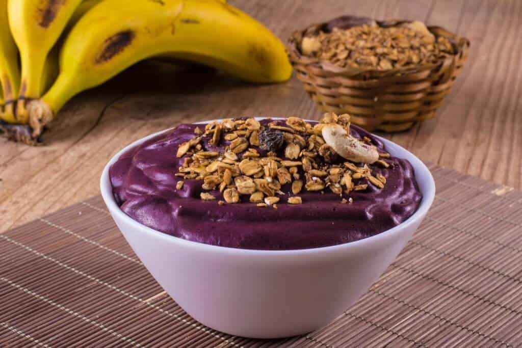 Tigela de açaí em primeiro plano e ao fundo cacho de bananas e granolas. Imagem ilustrativa do texto sobre franquia Maria AçaÍ.