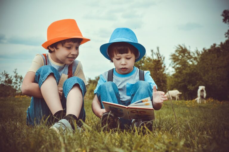 Duas crianças sentadas em um gramado lendo um livro. Imagem ilustrativa do texto mentalidade empreendedora das crianças.