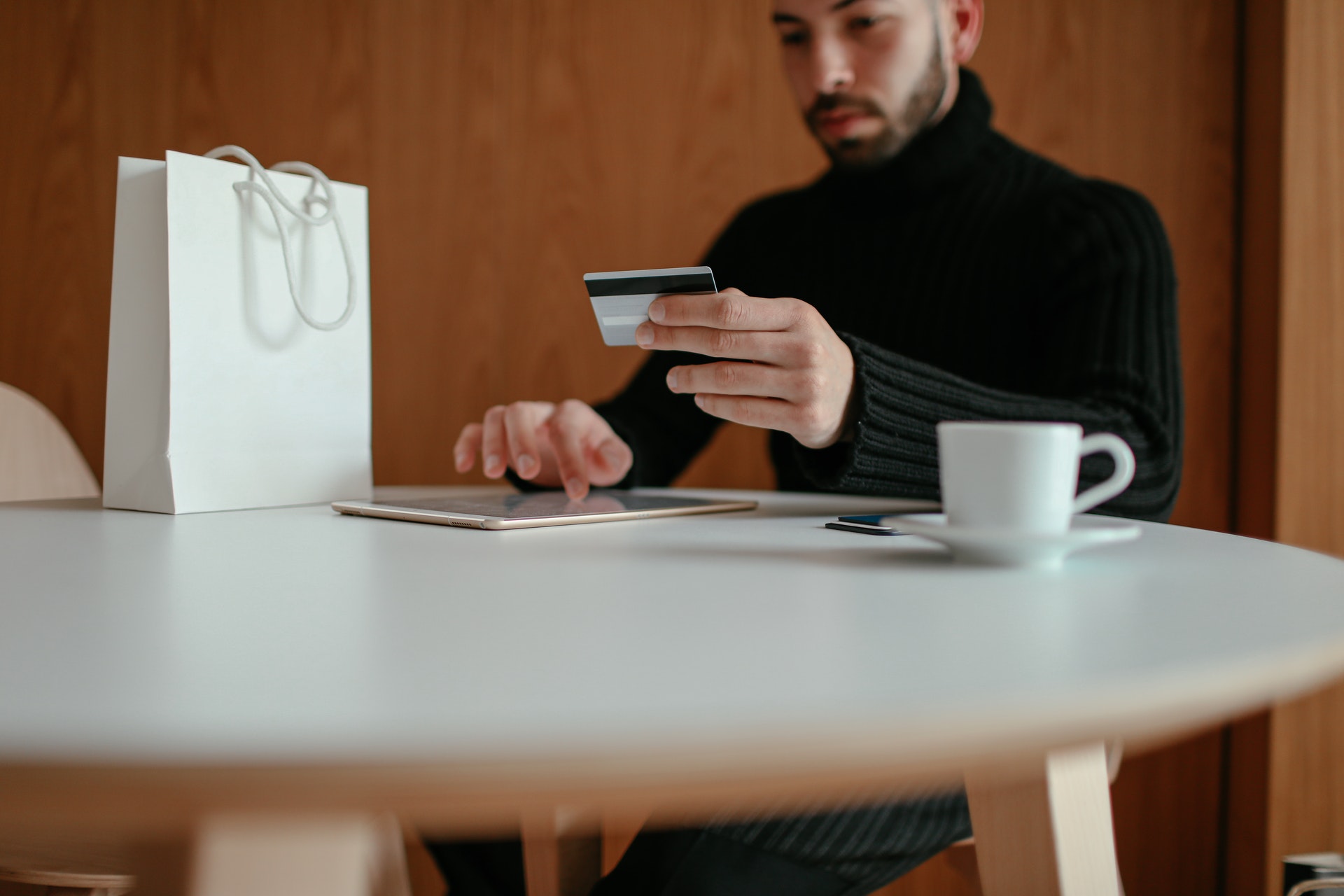 Homem sentando olhando para um cartão de crédito e mexendo em um tablet. Imagem ilustrativa do texto negócios rentáveis pouco investimento.