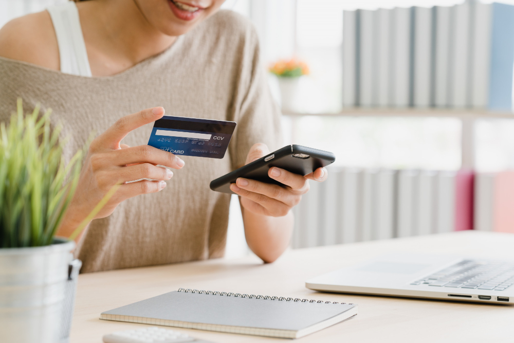 Mulher segurando cartão de crédito e celular. Ilustração do texto sobre franquias de sucesso baixo investimento.
