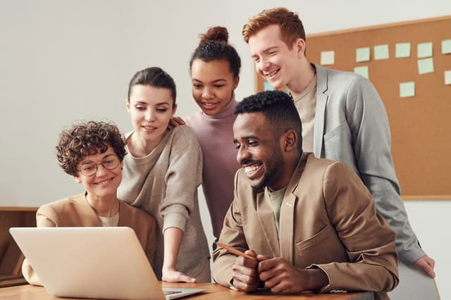 Grupo de pessoas sorrindo e olhando para notebook aberto. Ilustração do texto sobre como montar um negócio.