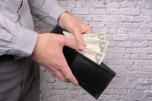 Mãos de um homem colocando notas de dólar em uma carteira preta. Imagem ilustrativa do texto razões para investir em franquia.