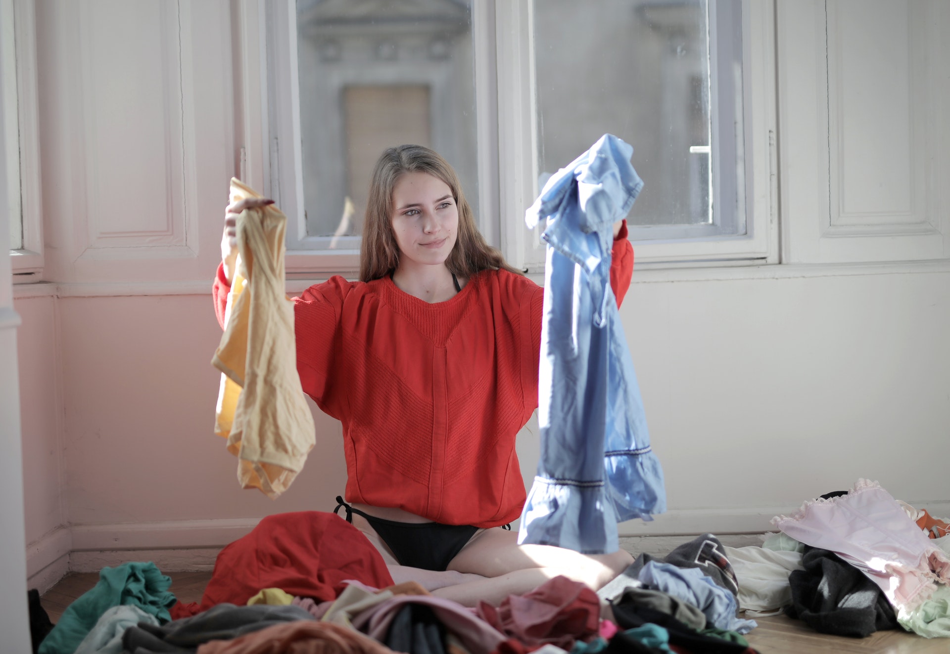 Mulher rodeada de roupas segurando peças em suas mãos. Imagem ilustrativa do texto sobre franquias para trabalhar na internet.