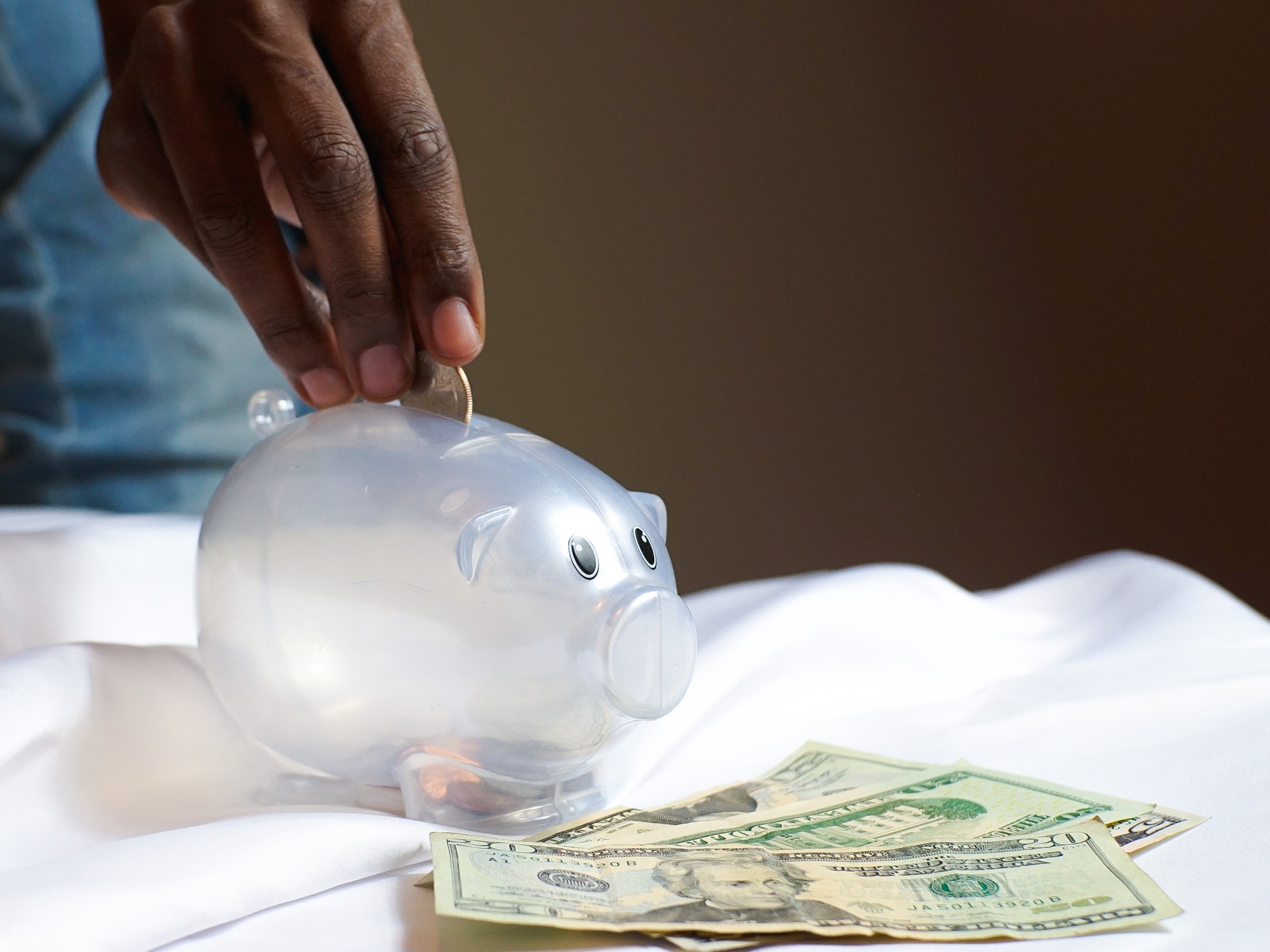 Mão colocando moedas em um cofre em formato de porco.  Imagem ilustrativa do texto sobre ideias de negócio próprio com baixo investimento.