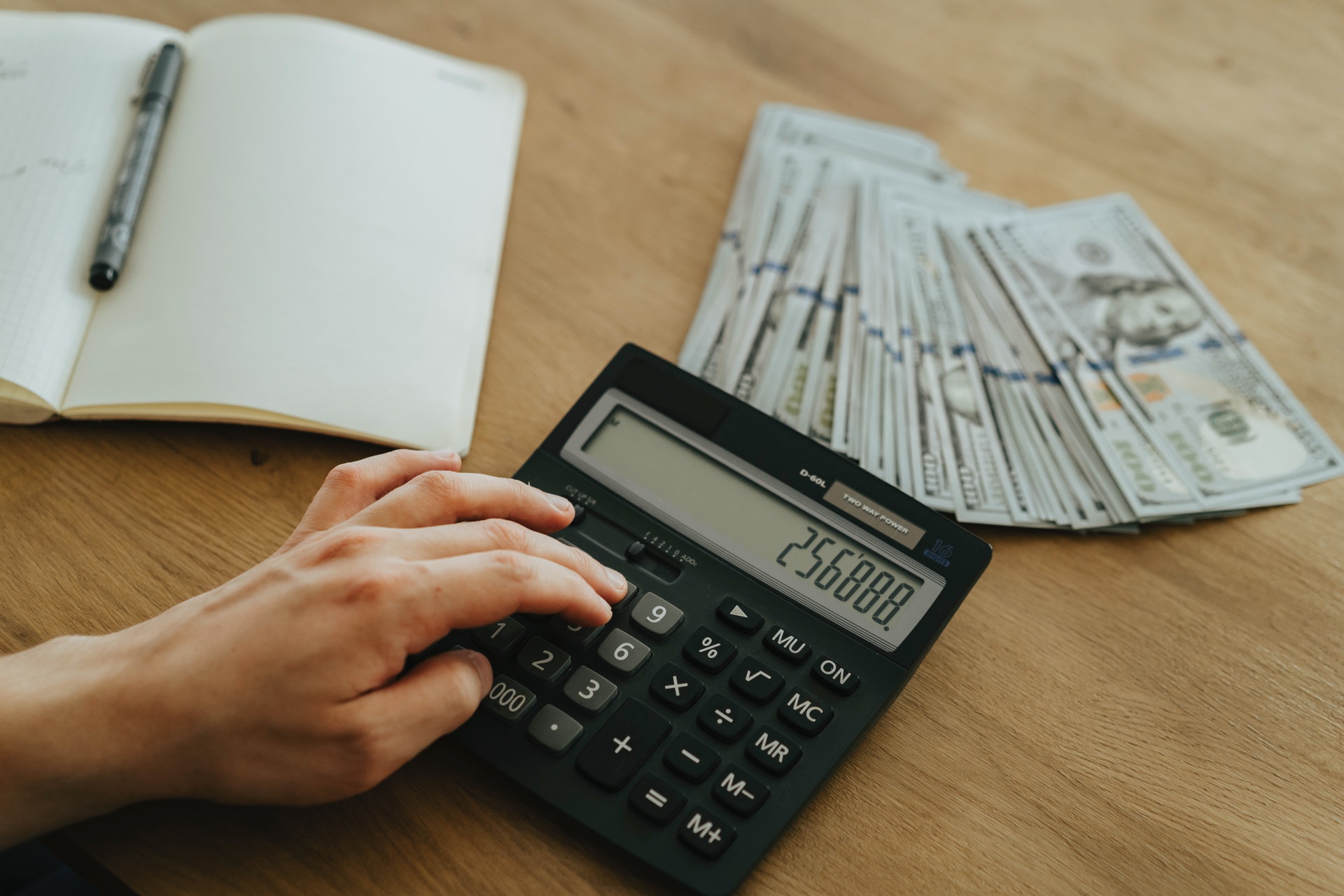 Mão sobre uma calculadora, com algumas notas ao lado e um caderno aberto. Imagem ilustrativa do texto sobre investimentos de baixo custo.