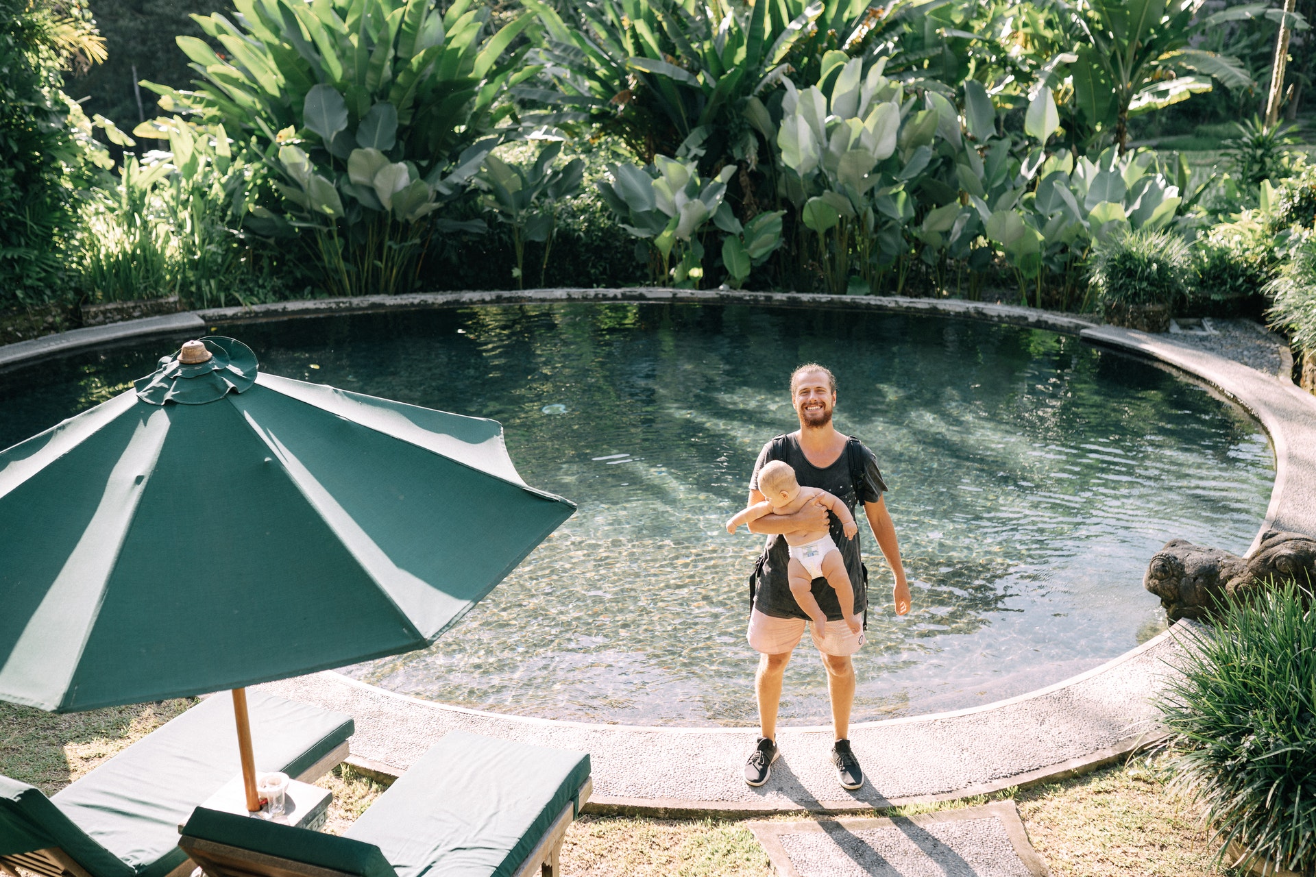 Homem segurando um bebê no colo em frente uma piscina. Imagem ilustrativa do texto melhores microfranquias do Brasil.