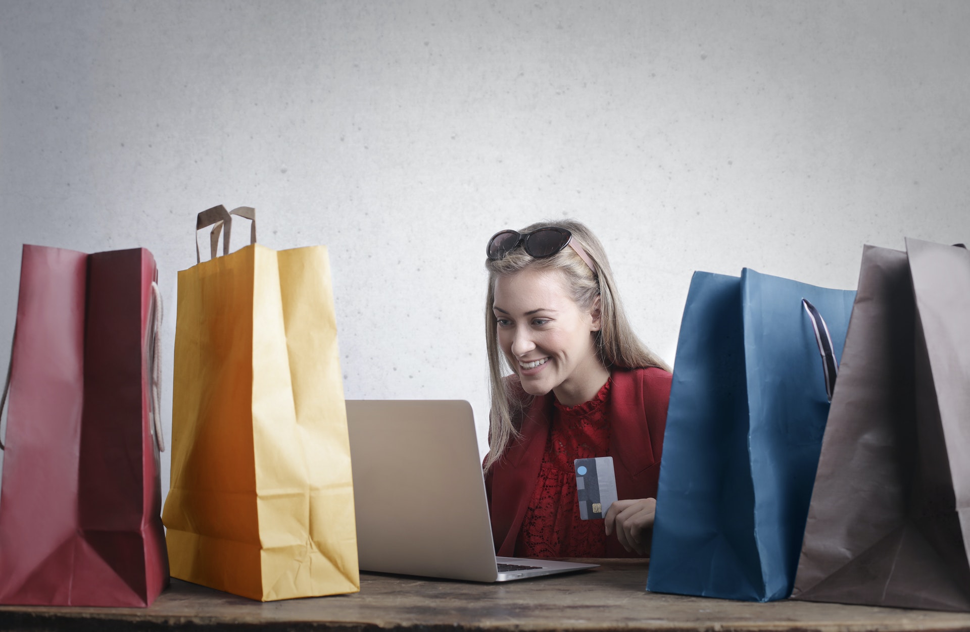 Mulher cercada por sacolas de compras em frente um computador. Imagem ilustrativa do texto sobre negocios online.
