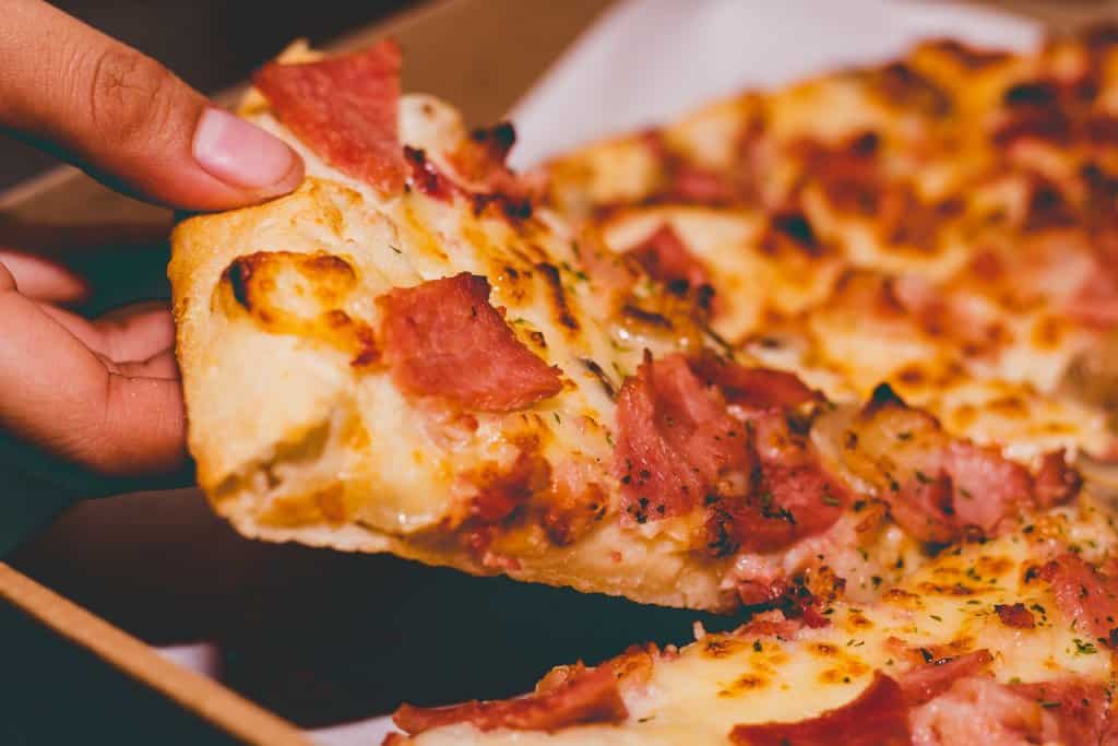 Imagem de uma fatia de pizza. Imagem ilustrativa texto franquia Dominos Pizza.