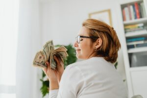 Mulher sorrindo e segurando várias notas de dinheiro. Imagem ilustrativa do texto negócio com pouco investimento.