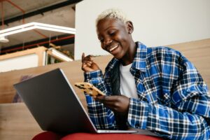 Mulher sorrindo segurando um celular e olhando para um computador. Imagem ilustrativa do texto sobre qual a melhor franquia para investir.
